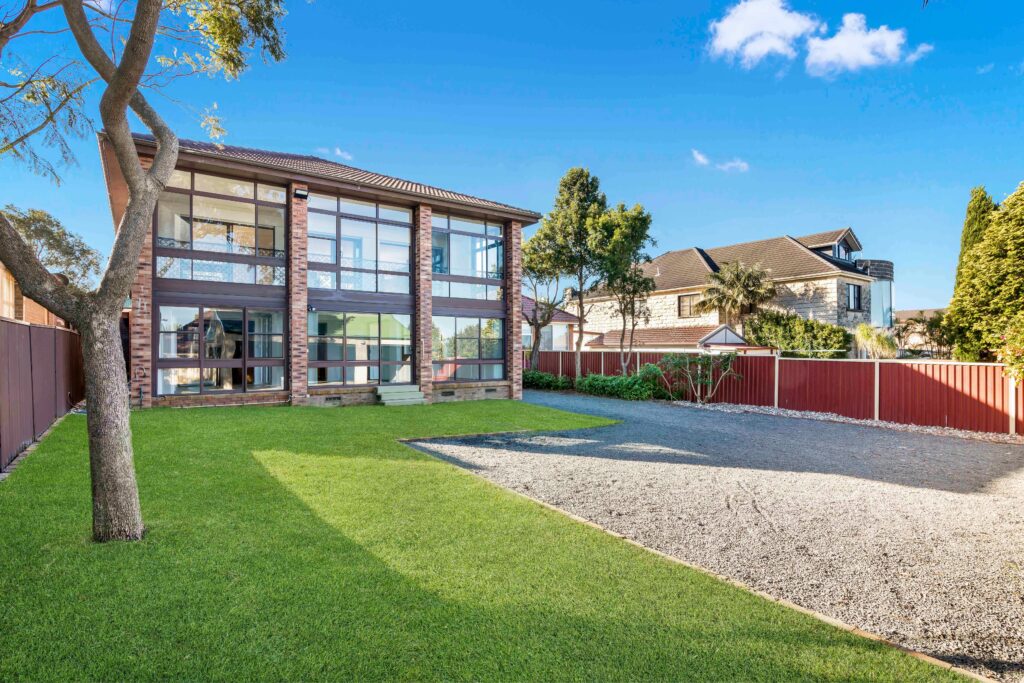 Modern two-story residential property with large windows, surrounded by green lawn and gravel driveway, located in Earlwood, available for rent at $1350 per week.