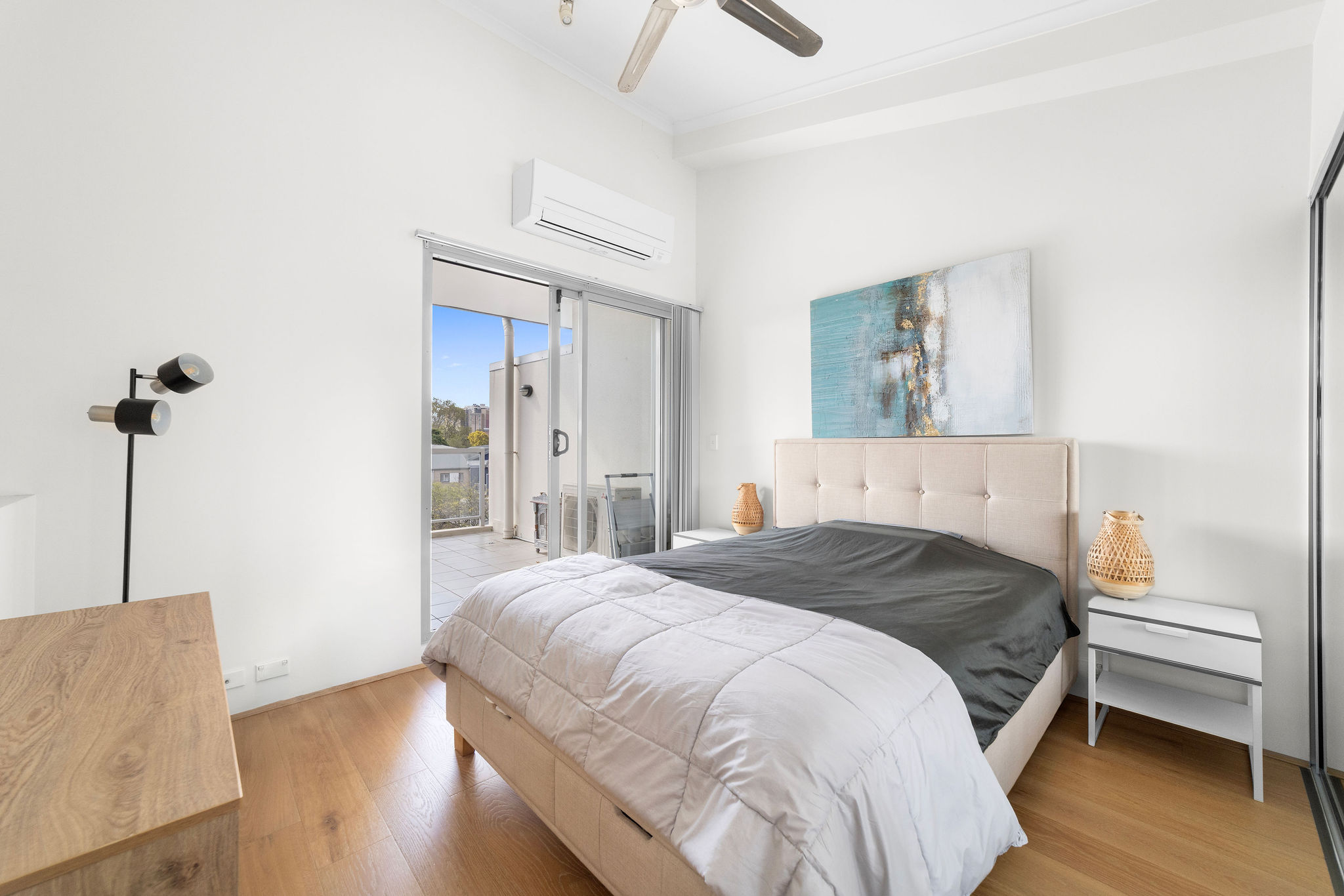 Stylish furnished bedroom in two-level loft, featuring a queen bed, modern decor, and balcony access with garden views.