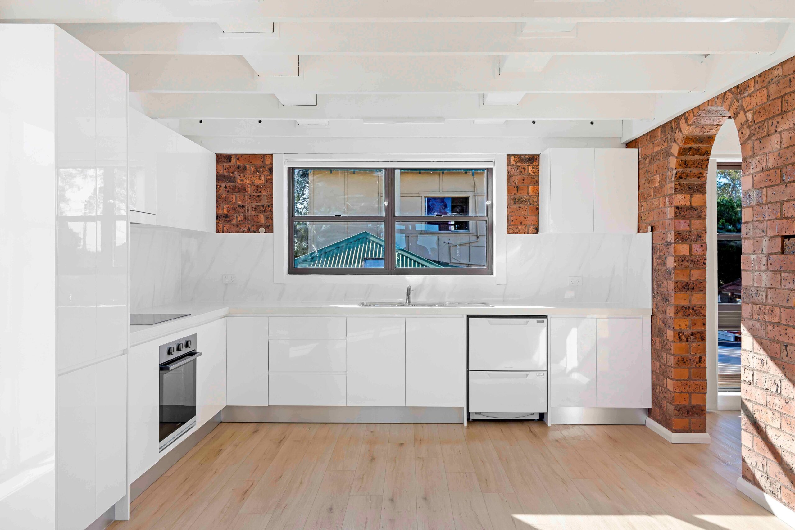Modern kitchen with white cabinetry, marble backsplash, and natural light from large window, showcasing spacious layout and contemporary design features in Earlwood property.