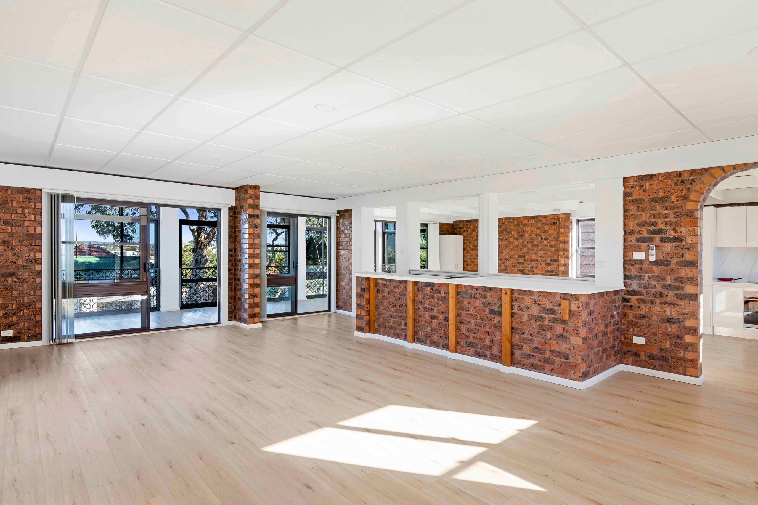Spacious living area with natural light, featuring brick walls, wooden accents, and open layout, ideal for comfort and entertaining in Earlwood rental property at 104a Bayview Avenue.