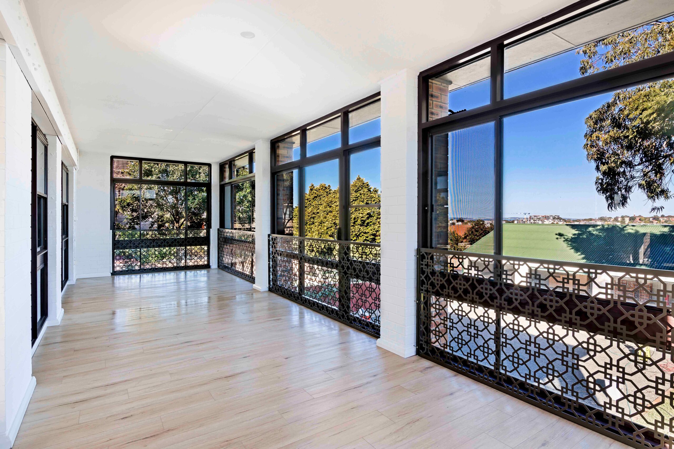 Spacious sunlit indoor balcony with large windows and decorative metal railings, showcasing views of greenery and neighboring rooftops, ideal for comfortable living in Earlwood.