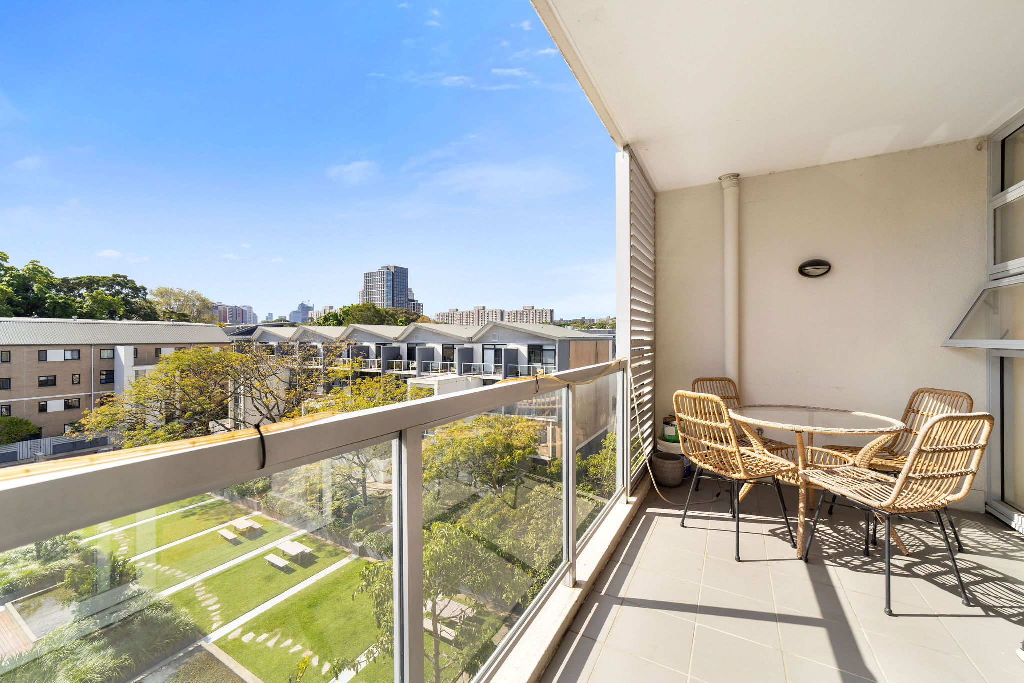 Stylish balcony with a round table and four chairs overlooking tranquil gardens and urban skyline in Alexandria, ideal for relaxed living.